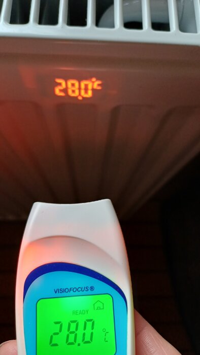 Termometer mäter temperaturen 28,0 °C på en radiator, visar både avläsning på skärmen och projicerad siffra.