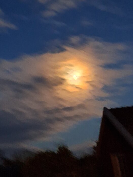 Månen syns genom moln på en skymningshimmel ovanför ett hustak klockan 17.