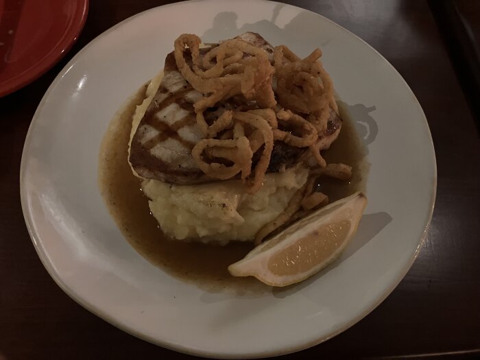 Rätt-tillagad svärdfisk på potatismos, toppad med friterad lök och serverad med en citronklyfta.