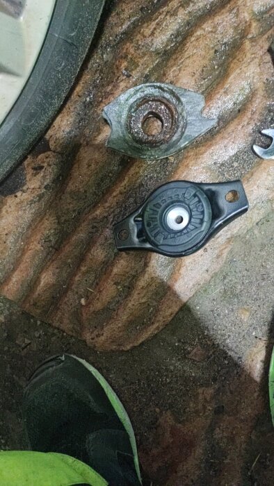 Trasigt dämparfäste för Volvo V60 på marken, nära hjul och verktyg, efter utförd reparationsinsats.