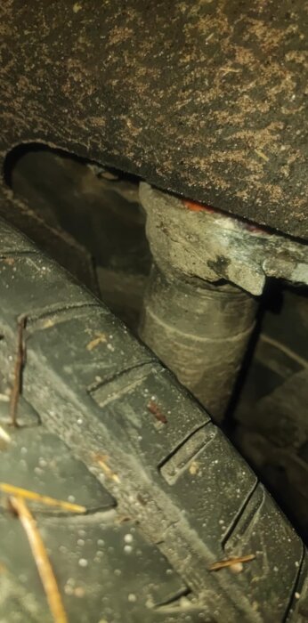 Närbild av dämparfästet och delen av ett däck på en bil, med rostfläckar synliga på metallen runt infästningen.