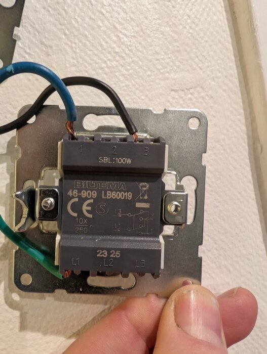 Elektrisk kopplingsenhet med svarta och blå kablar, märkt "Biltema 46-909 LB60019", fastsatt i vägg med skruvar.