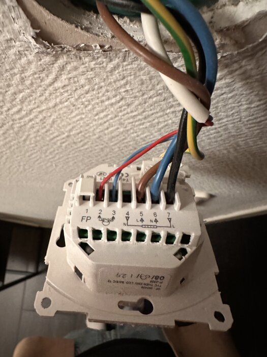Gammal T2 termostat med öppning för elektriska kopplingar, flera kablar synliga och inkopplade, mot en monteringsplatta på vägg.