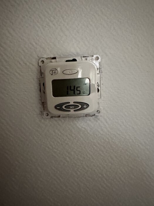 Gammal T2 termostat monterad på väggen, visar temperaturen 14,5 grader Celsius.