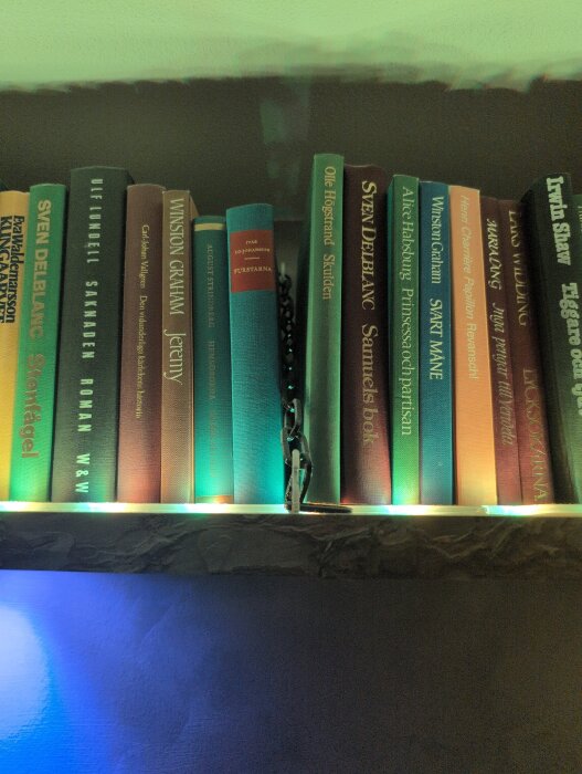 Hyllplan med böcker på en gipsvägg, upphängda med beslag närmast väggen och en kedja i 45 graders vinkel, fästa för att bära lasten.