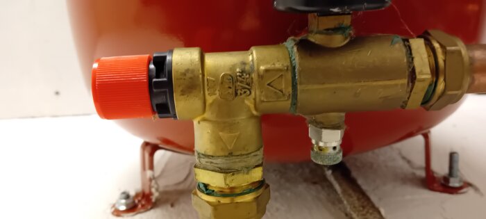 Säkerhetsventil med röd plastkåpa på ett kopparrörssystem, del av bergvärmeanläggning.