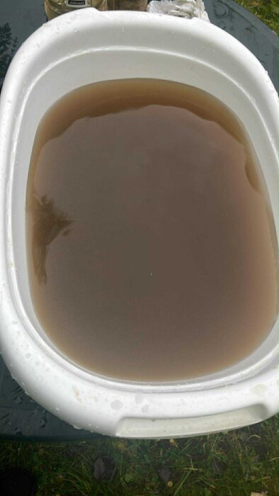 Brunt, grumligt vatten i vit plastbalja efter rengöring av kolfilter i brunn.