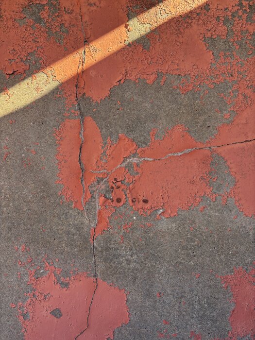 Bilden visar en balkongyta med röd färg som flagnar och synliga sprickor i betongen.