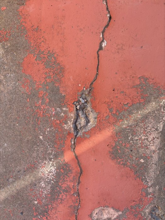 Spricka i röd balkongbetong med flagnande yta och synlig grå spricka som behöver åtgärdas.