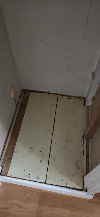 Äldre garderobsgolvet med borttagen plastmatta, visar träplankor och vägguttag vid kanten, efter oro för eventuell asbest.