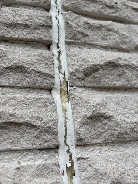 Fog mellan mexitegelstenar på fasad med synlig glipa och sprickor, delvis täckt av vit fogmassa.