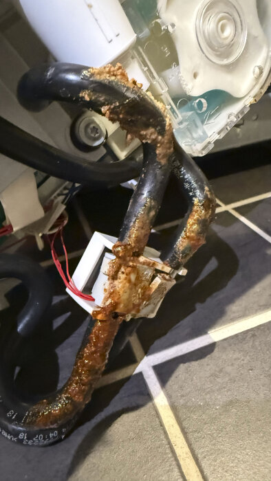 Rostiga slangar och komponenter i en tvättmaskin efter vattenläckage, med rostbrun beläggning synlig på rören och plastdelarna.