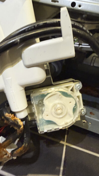 Insidan av en tvättmaskin med rostbruna avlagringar och vittrade plastdelar runt pumpar och slangar.