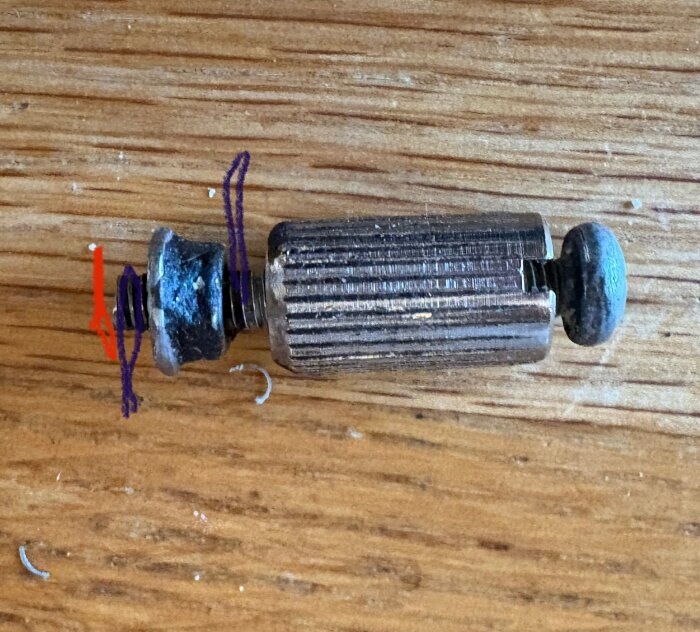 Närbild av skruvkonstruktion på träbord, med en avskuren skruv till vänster markerad med röd och lila pil, och torxhuvud till höger.