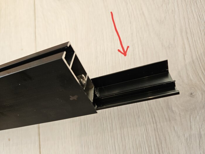 Närbild på en svart ramdel som sticker ut från Ikea Skyttapanel, med en röd pil markerande den utdragbara delen.