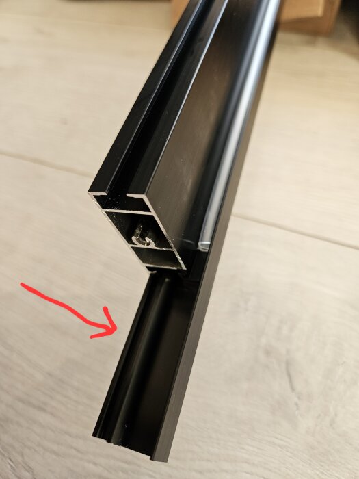 Närbild av en svart, L-formad metallprofil från IKEA Skytta, med en röd pil som pekar på en utstickande del av ramen.