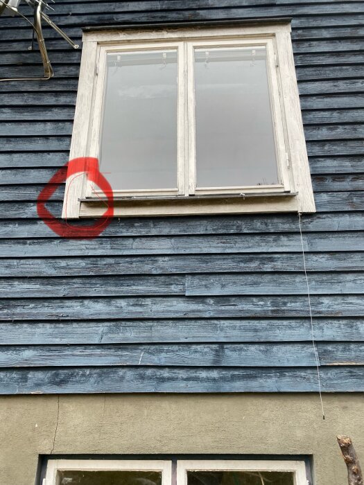 Fönster på blå träfasad med röd markering kring skadad list, potentiellt problemområde enligt användarinlägget om byggfel.