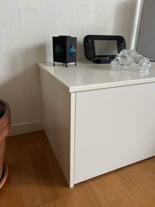 Vit IKEA Bestå tv-möbel mot en vägg, dekorerad med en svart kubformad prydnad och en genomskinlig glasfigur.