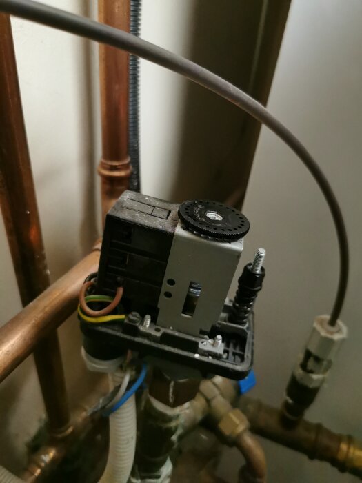 En installation med kopparrör, en svart ratt och en liten skruv synliga.