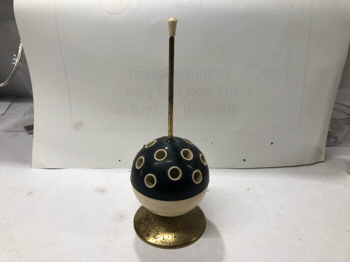 Bordsställ för cigaretter med inbyggt urverk, cirkelformad dekor med flera hål ovanpå och placerat på ett bord.