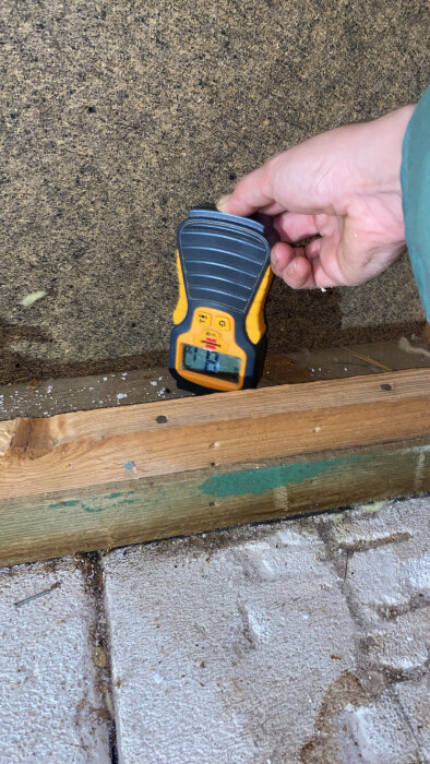 Fuktmätare används mot en vägg nära golvet för att mäta fuktighet i ett byggprojekt.