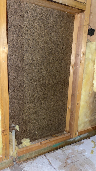 En vägg med isolering och träreglar nära golvet, spår av fukt synliga på träet.
