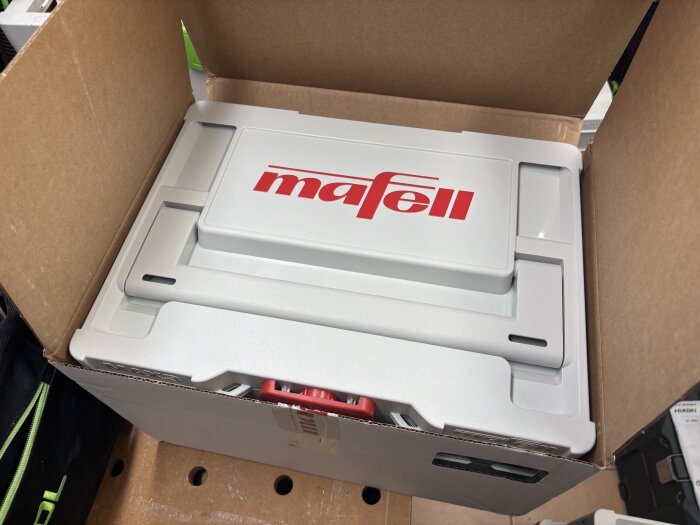 En ny Mafell-maskin i en öppen kartonglåda, sedd uppifrån.