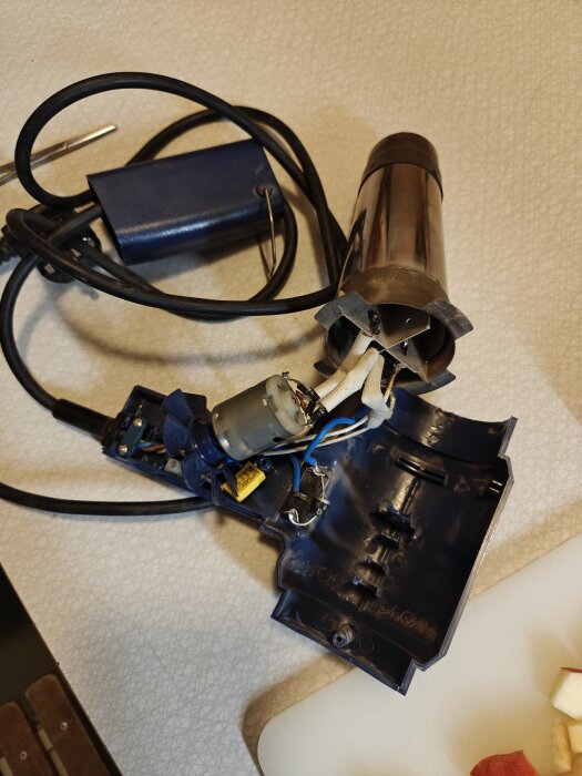 Öppen varmluftspistol med synlig inre mekanik och ledningar, visas under reparation med lödning och skarvning av kablar.