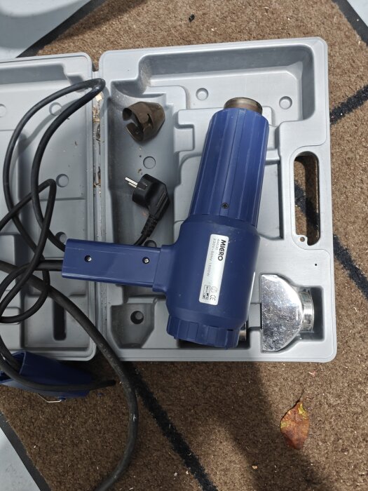 Blå varmluftspistol i en öppen förvaringslåda med sladd och flera tillbehör.