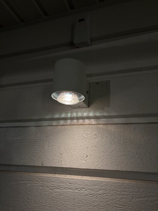 Vägglampa i carport med inbyggd spotlight som lyser upp väggen.