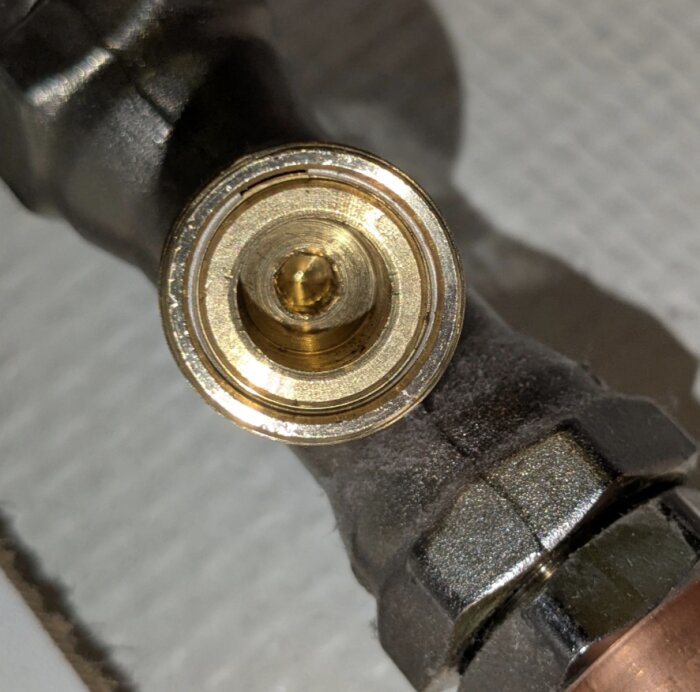 Guldfärgad ventil på radiatorkrets, närbild av ventilmutter. Liknar strypventil med insexanslutning för eventuell injustering eller avstängning.