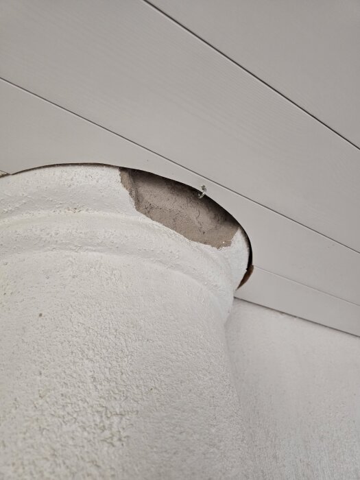 Vitmålad och flagnande vägg med synlig puts under i hörn.