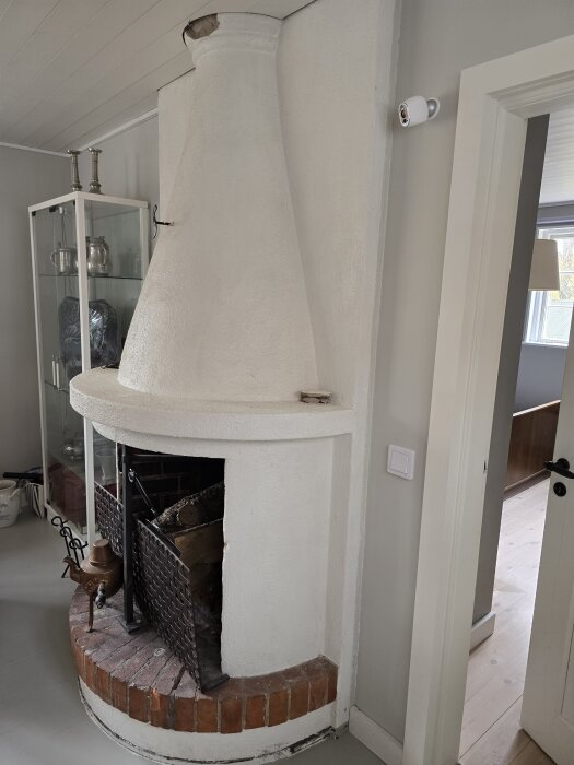 Vitmålad öppen spis med murad bas och trädetaljer i modern inredning; diskussion om färgborttagning och putsbevarande.