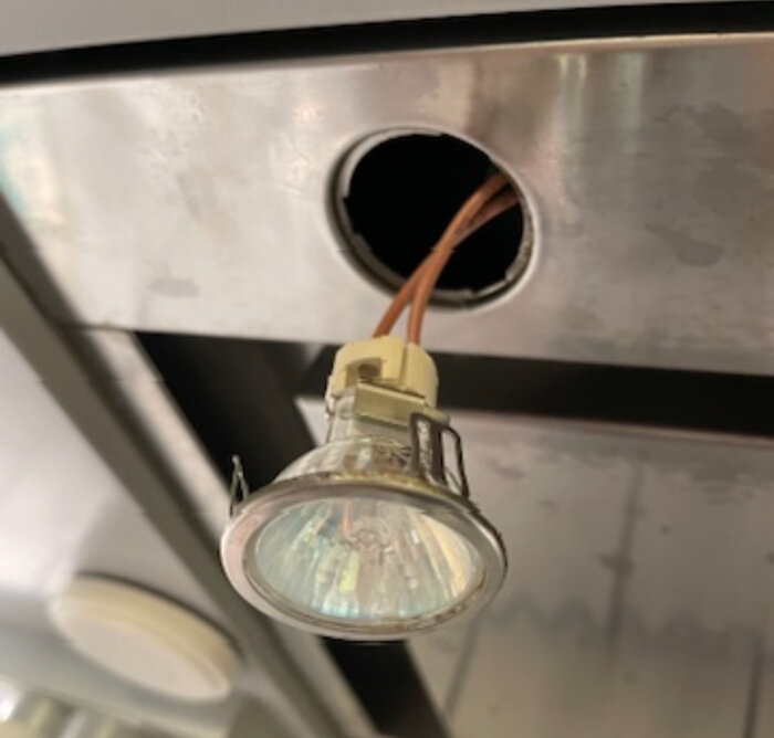 En halogenlampa hänger ner från ett öppet hål i ett metalltak, med kabeln synlig.