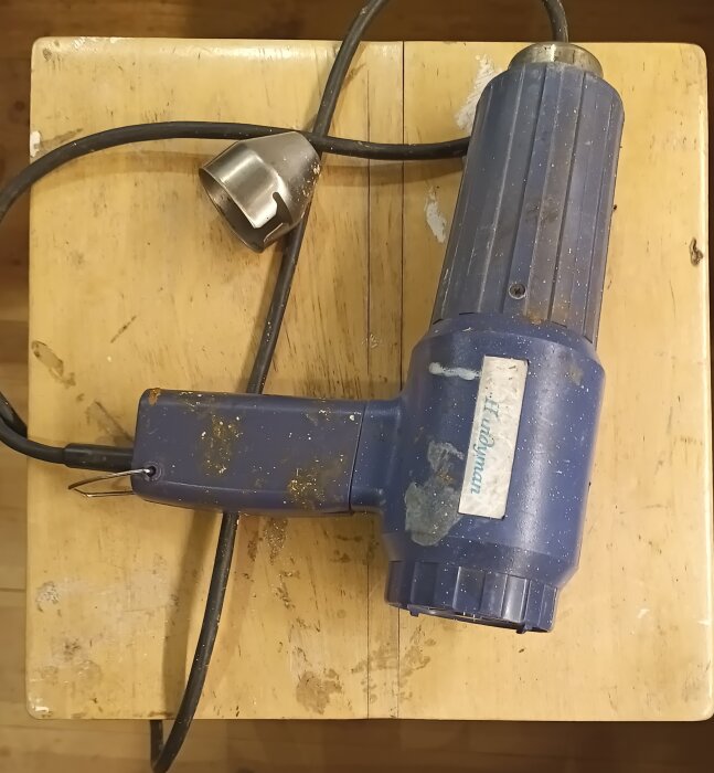 Blå värmepistol av märket Handyman, sliten och placerad på en träyta.