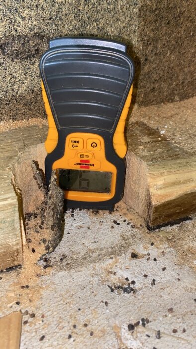 Fuktmätare placerad på trägolv nära en spricka, används för att kontrollera eventuell vattenskada under ett gammalt vinylgolv i köket.