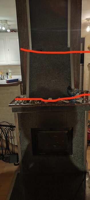 Kamin i sten med eldstad nederst och dekorationer av stenar och föremål ovanpå. Röda linjer markerar delar av designen.