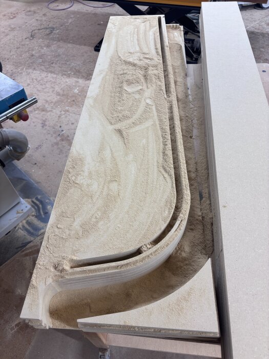 Svängda socklar av 7 lager tricoya, täckta av sågspån efter fräsning, på en arbetsbänk i en verkstad.