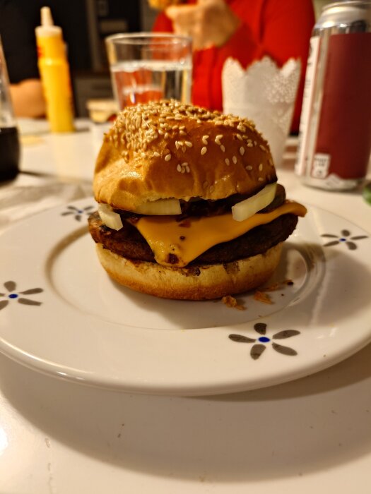Hamburgare med ost och lök på en vit blomsterdekorerad tallrik.