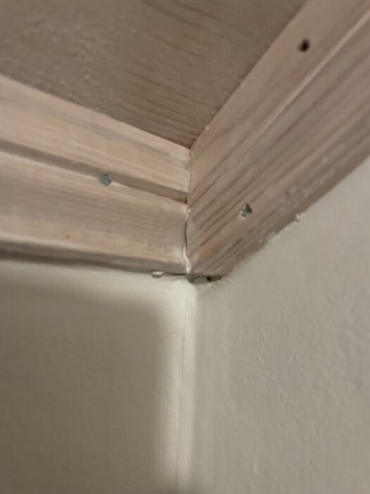 Hörn av träsockel monterad i ett rum, skruvad i väggen och taket.