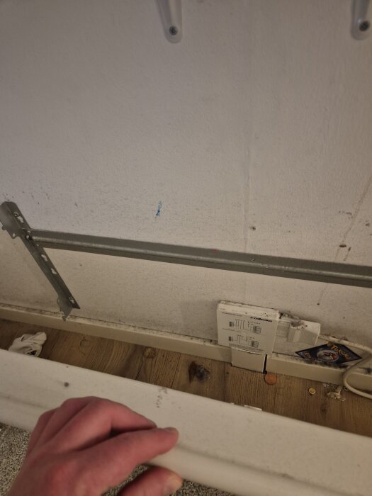 Väggmonterad enhet av märket a-collection ovanför ett trägolv med diverse småföremål inklusive ett Pokémon-kort och en hand som håller i ett element.