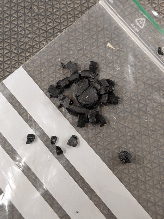 Svarta plastbitar från en trasig dyckertpistolens rekyl-dämpare ligger utspridda på en plastpåse med vitt mönster.