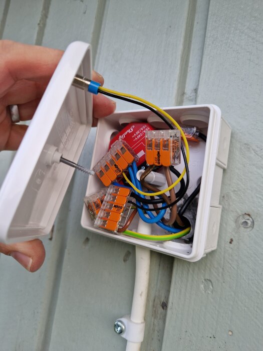 En öppen kopplingsdosa med flera kablar, inklusive röda och gula, monterad på en yttervägg i trä.