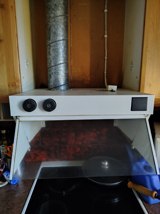 Köksfläkt från 70-talet med plåtrör och glaslucka monterad ovanför en spis i ett äldre kök.