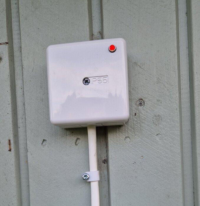 Vit P55-elbox monterad på vägg med röd lysdiod indikerande påslagen status, kopplad med kabel nedåt.