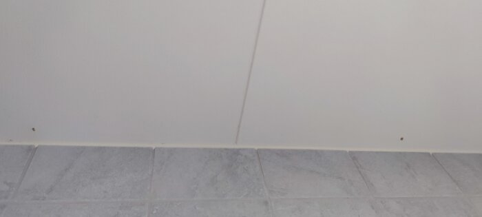 Två fläckar i linje på vitt innertak ovanför grått kakelgolv.