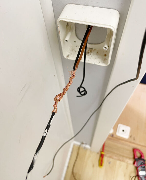 Öppen väggdosa med blottade kopparledningar i ett eluttag under renoveringsarbete, vilket visar felkopplad dimmer.