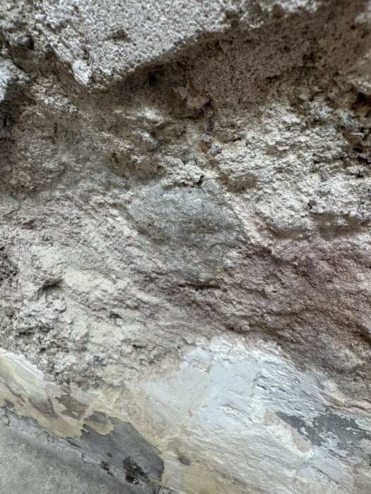 Nära bild på gammal murvägg där delar av putsen har vittrat bort, avslöjande underliggande material av stenblock och grus.