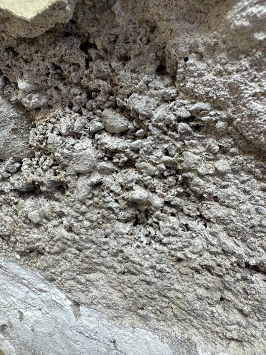 Vittrad puts med synlig grund av stenblock och smågrus i en källarvägg från 40-talet. Fuktproblem med puts som lossnar nedtill.