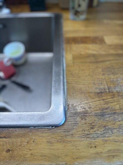 Bild av en diskbänk med rostfria kanter och en träskiva som visar tecken på vattenskada nära fogen.